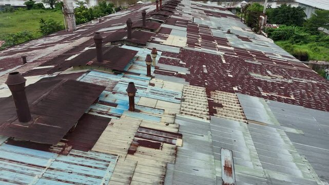 A rusted corrugated metal factory roof with a chimney vent and weathered, patchwork panels atop an industrial building.