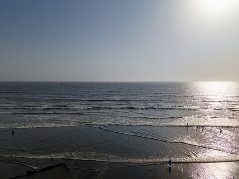 Aerial view of Sea-View Beach with gentle waves rolling onto the sandy shore and people walking along the water in Karachi, Sindh, Pakistan.