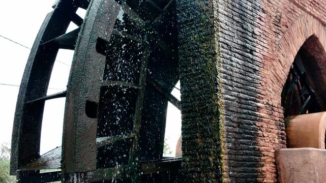 Historic iron waterwheel of Rueda de la &Ntilde;ora spinning and splashing water next to an ancient red brick aqueduct structure in Alcantarilla Murcia Spain showcasing traditional agricultural engineering 