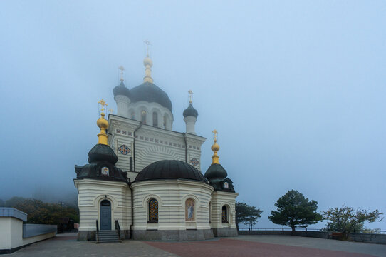 Picturesque Orthodox Church of Resurrection of Christ with white walls and black domes topped with golden crosses. Foggy weather, adding mystery to scene.  Foros, Crimea