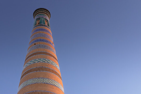 Islam Khoja minaret in Khiva with ornate glazed tile bands rises against a clear blue sky. This iconic Uzbekistan landmark image suits travel brochures and cultural publications.