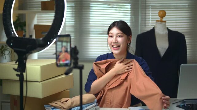 Young Asian Woman Live Streaming Fashion Sales from Home Office with Ring Light and Smartphone