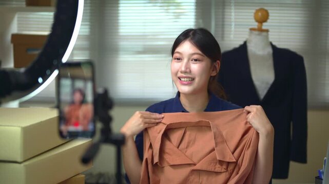 Young Asian Woman Live Streaming Fashion Sales from Home Office with Ring Light and Smartphone