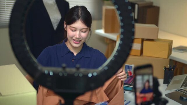 Young Asian Woman Live Streaming Fashion Sales from Home Office with Ring Light and Smartphone