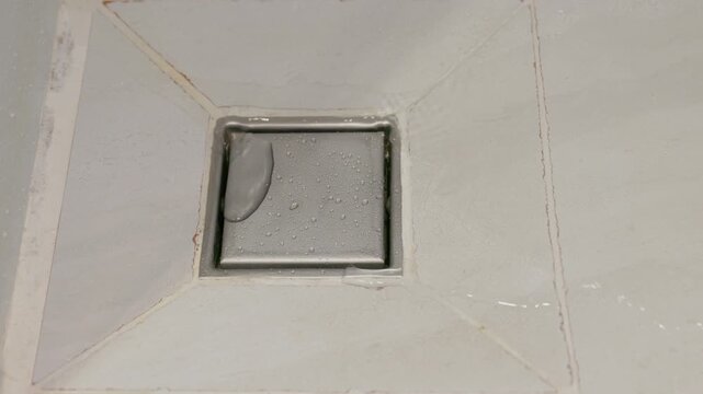 Stainless steel square floor drain in bathroom.