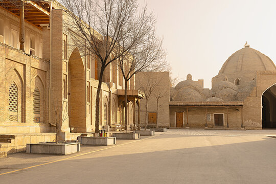 Toqi Zargaron trading dome and historic brick buildings in Bukhara on a quiet winter morning. Empty courtyard with bare trees and pointed arches conveys the timeless atmosphere of the old town.
