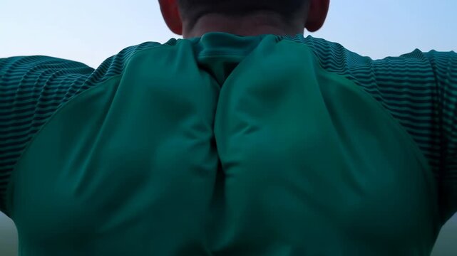 Rear view athlete in teal jersey tightening shoulders on foggy sports field at dawn