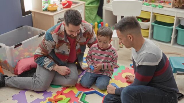 Boy plays with wooden blocks as two men kneel and guide him inside a building; learning connection warmth.
