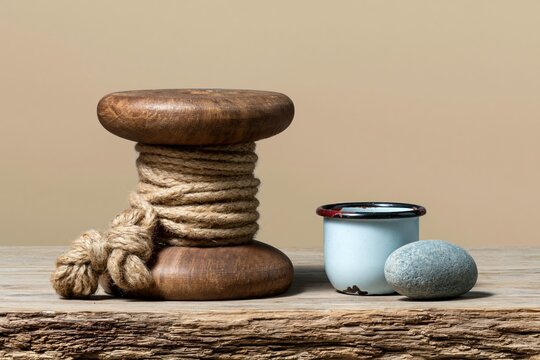 Weathered wooden kite spool with tangled natural twine sits on a sun-bleached dock surface with an enamel cup for nostalgic outdoor and lifestyle branding