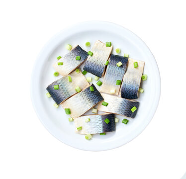 Herring pieces with green onions on a white ceramic plate isolated on a white background, top view.