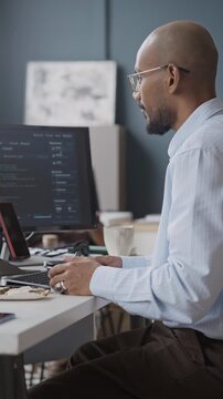 Vertical side view shot of young Indian male developer eating lunch at office desk while coding on computer. Clip is ideal for IT recruitment and software engineering promotional videos
