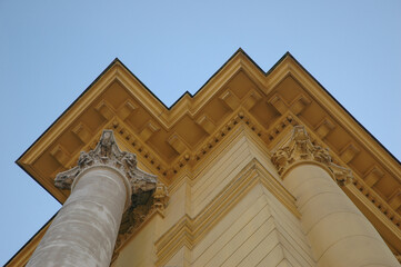 Low angle view of a neoclassical building facade showing prominent roof cornice molding supported by decorative pillars against clear blue sky. © nahhan