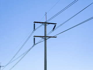 Obraz premium A tall concrete utility pole supports high voltage power transmission lines with ceramic insulators against a clear blue sky.