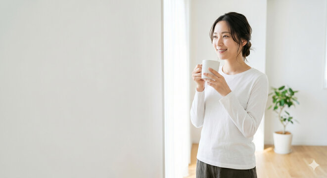 朝の白い部屋で温かい白湯を飲み、ホッとリラックスする20代女性