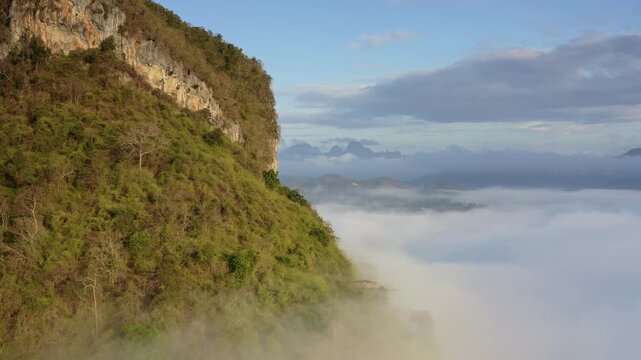 Khao Sok National Park, aerial drone flight over stunning limestone karsts rising above thick layer of morning fog and clouds, lush tropical mountains against the vibrant blue sky in Thailand