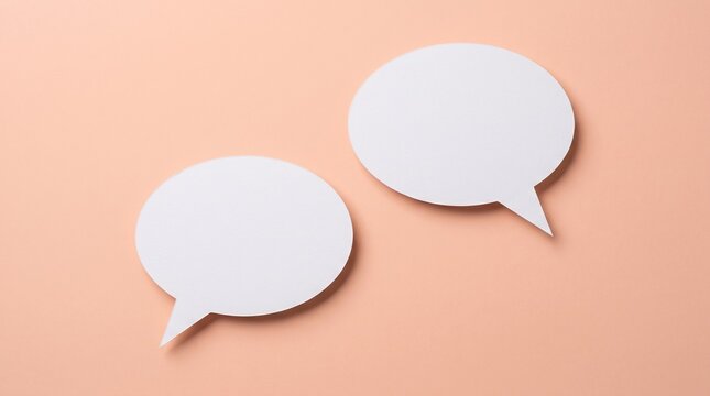 Two blank white paper speech bubbles featuring a smooth matte texture arranged in a simple minimalist composition against a soft pastel peach colored flat background