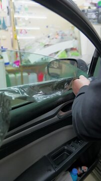Professional removal of dark tinting film from a car side window in a detailing workshop. Close-up of hands peeling off the layer. Vertical video