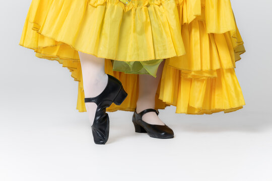 Character dancer feet in black dance shoes and yellow skirt close up on white background