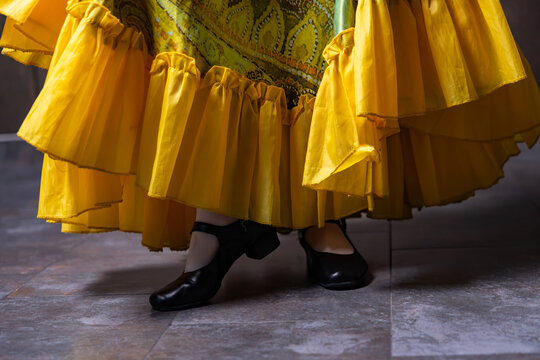 Character dancer feet in black stage shoes and ruffled yellow skirt close up on tiled floor