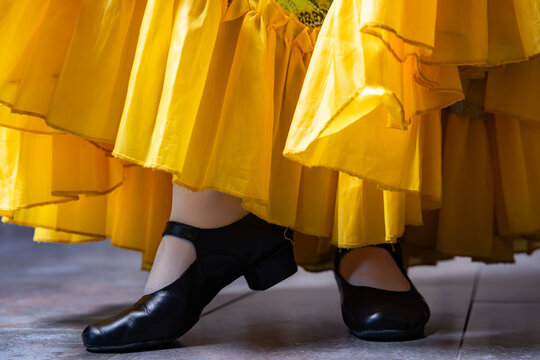 Character dancer feet in black stage shoes and ruffled yellow skirt close up on tiled floor
