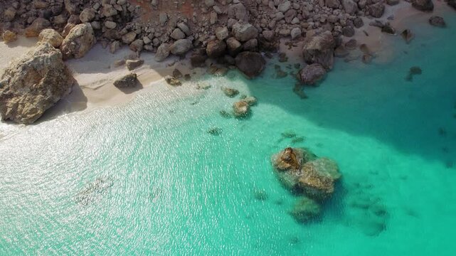 Aerial view of rocky shoreline and clear emerald sea water on a secluded pebble beach