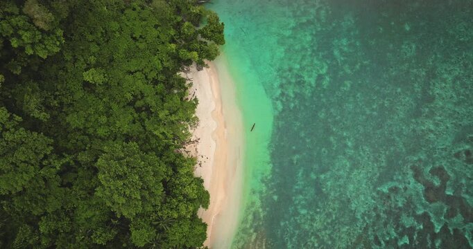 Tropical nature travel background. Lush green jungle forest meets pristine white sand and shallow turquoise water revealing a vibrant underwater coral reef, small traditional boat resting on the shore