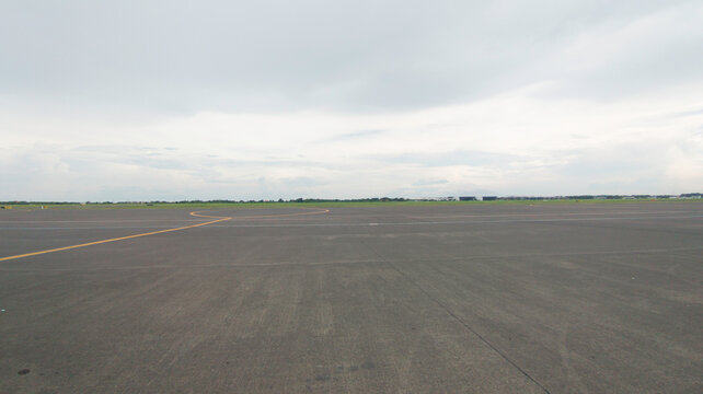 Wide Open Empty Asphalt Runway Tarmac with Yellow Line under an Overcast Cloudy Grey Sky