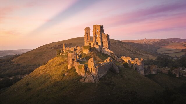 Sitting ruined stone castle catching warm sunlight on rounded hilltop, with winding footpath