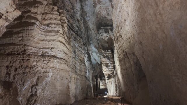 Massive limestone cave chamber with illuminated rock walls and walking path in Sardinia