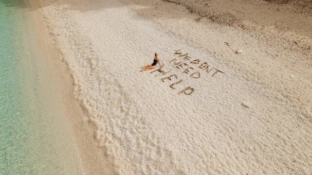 Woman relaxing on quiet Kefalonia shore beside playful phrase we dont need help in sand