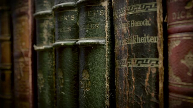 Worn antique books with embossed leather covers and aged pages arranged on a wooden surface with warm soft indoor lighting.
