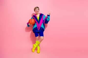 Retro-inspired athlete posing with a basketball in vibrant stylish activewear and windbreaker against a pink backdrop © deagreez