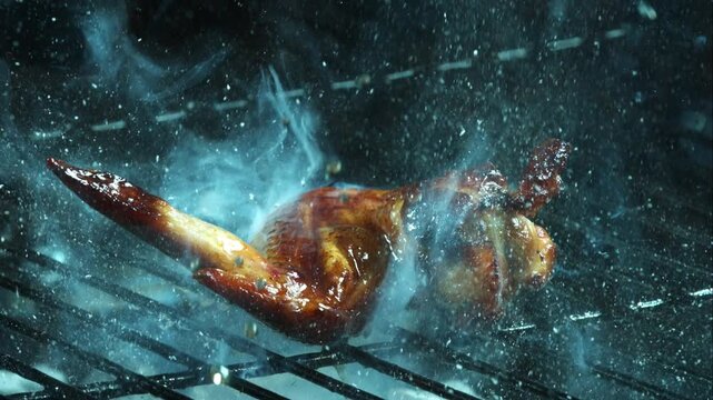 Delicious roasted chicken wing grilling on hot barbecue grate with rising smoke and flying droplets of tasty sauce