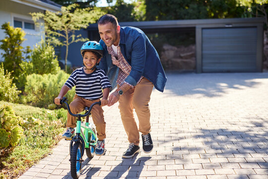 Happy smiling father helping son riding bike outdoor