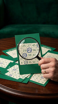 Hand with ring holding magnifying glass over lottery tickets, representing chance, luck, and anticipation for winning