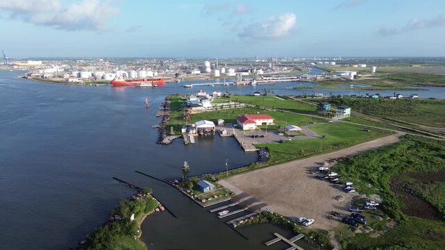 Public boat ramps parking lots sit adjacent to Harbor, overlooking industrial terminals. Morning sunlight highlights red roof structures, grassy fields, docked small boats, Freeport, Texas
