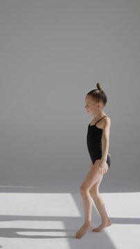 Little Caucasian girl gymnast in a black leotard posing on a white background. 