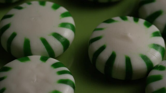 Macro close up of round white peppermint candies with green stripes sitting on a bright lime green background