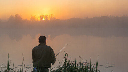 fisherman stands by a misty lake at sunrise, holding a fishing rod amidst tall grass under a golden sky © Александр Арендарь