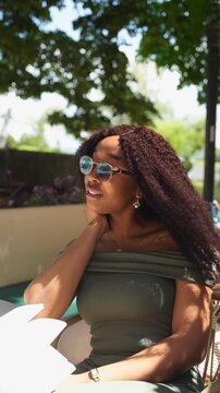 Young and beautiful black woman drinking water in a cafe and reading a book on a sunny and windy day