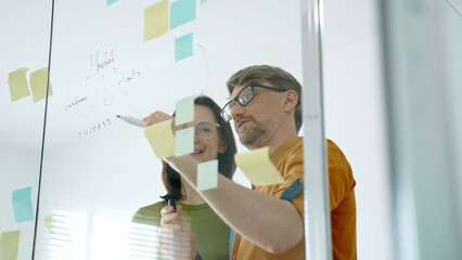 Business colleagues brainstorming innovative ideas during agile meeting, discussing project strategy, developing creative solutions with sticky notes on glass wall in modern office © Hanna