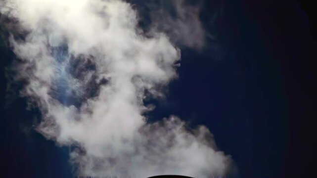 Steam plume rises under focused beam in dark industrial setting, forming dense white vapor against black background for pollution, ventilation, energy production, climate impact and emission control.