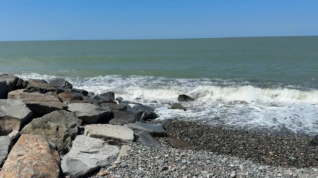 Ocean waves crash against rocky shore under clear blue sky, ideal for background or banner use