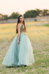 Fototapeta premium Young woman in formal gown standing in ﬁeld during golden hour vertical