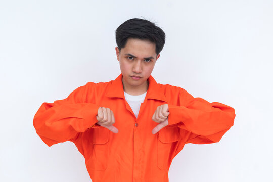 Young male seafarer in orange coveralls giving a double thumbs down gesture in a half body portrait, expressing disapproval, dissatisfaction, or negative feedback.