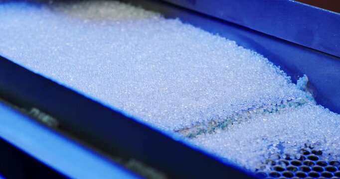 Close-up view of small transparent plastic pellets vibrating on a metal industrial sieve machine