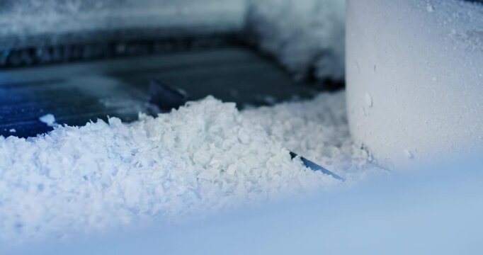 Close up of granulated white material being moved on a vibrating metal conveyor belt in a factory setting