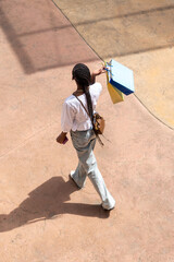 top view of afro woman with long dark braids, wearing a white lace blouse and jeans, standing with bags on a street or shopping center © Inspiraciones