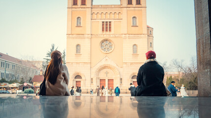 People sitting on plaza looking at a historic European-style cathedral in Qingdao © nhat.photograph