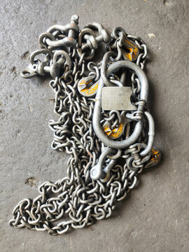 A heavy-duty industrial alloy steel lifting chain sling with master link, clevis shackles, and grab hooks on a concrete workshop floor.
